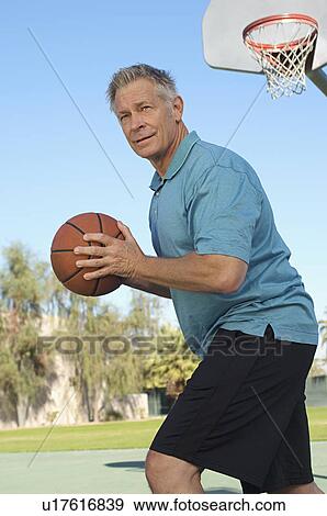 Stock Photo - Senior man playing basketball on outdoor court. Fotosearch
