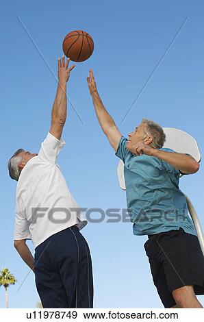 Stock Photo - Senior men playing basketball on outdoor court. Fotosearch