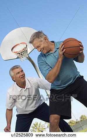 Stock Photo - Senior men playing basketball on outdoor court. Fotosearch