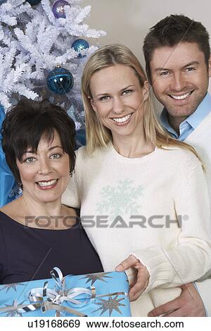 Stock Photo - Senior woman and mid adult couple in front of Christmas tree, portrait. Fotosearch