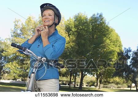 Stock Photo - Senior woman fixing bicycle helmet. Fotosearch