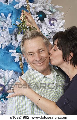 Stock Image - Senior woman kissing man under mistletoe. Fotosearch