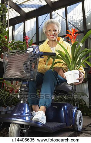 Stock Photography - Senior woman on motor scooter in garden center. Fotosearch