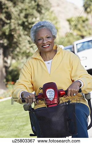 Stock Photo - Senior woman on motor scooter on urban street. Fotosearch