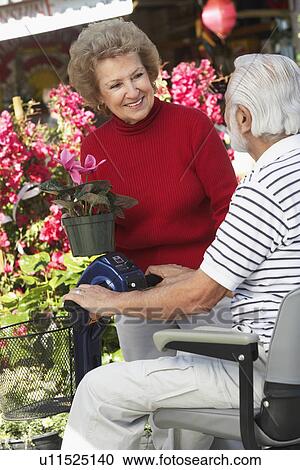 Stock Image - Senior woman talking with elderly man on motor scooter in garden center. Fotosearch