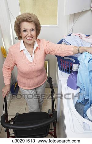 Stock Image - Senior woman with laundry by washing machine. Fotosearch