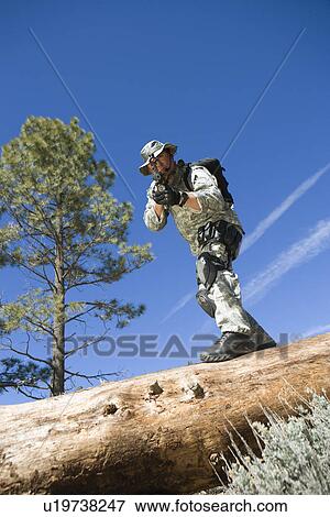 Stock Photo - Soldier pointing rifle from tree trunk. Fotosearch