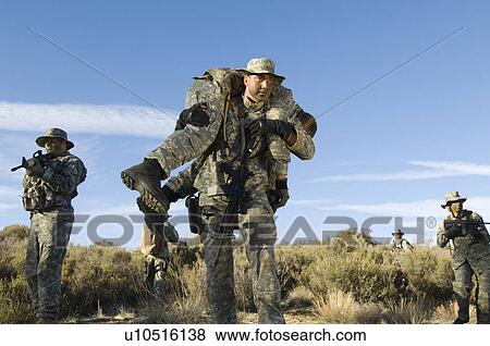 Soldiers walking in field, one carrying colleague View Large Photo Image Stock Photo - Soldiers walking in field, one carrying colleague. Fotosearch
