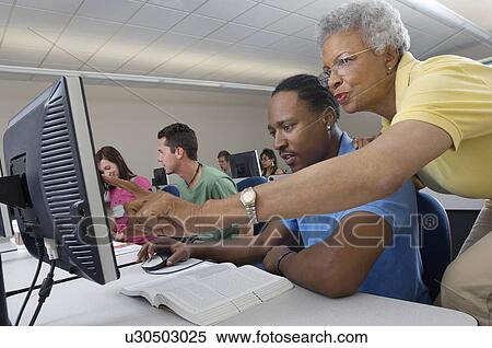 Teacher helping student in computer class View Large Photo Image Stock Photography - Teacher helping student in computer class. Fotosearch