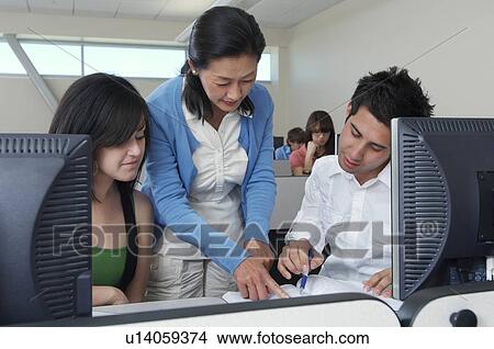 Picture - Teacher helping two students working in computer classroom. Fotosearch