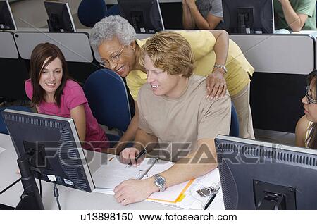 Stock Image - Teacher helping two students working in computer classroom. Fotosearch