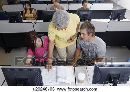 Stock Image - Teacher helping two students working in computer classroom. Fotosearch