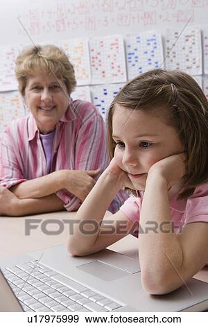 Stock Photo - Teacher Watching Schoolgirl Use Laptop. Fotosearch