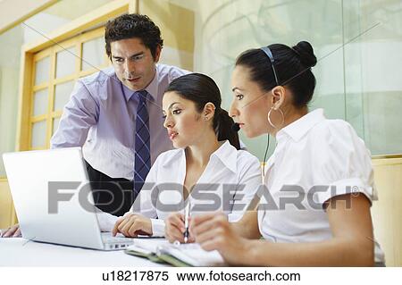 Stock Photography - Three business colleagues using laptop in office. Fotosearch