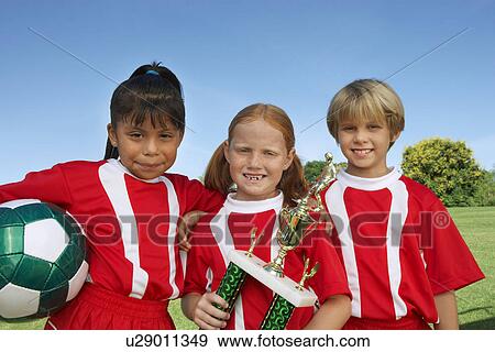 Three children (7-9 years) holding soccer ball and trophy on soccer field, portrait View Large Photo Image Stock Photo - Three children (7-9 years) holding soccer ball and trophy on soccer field, portrait. Fotosearch