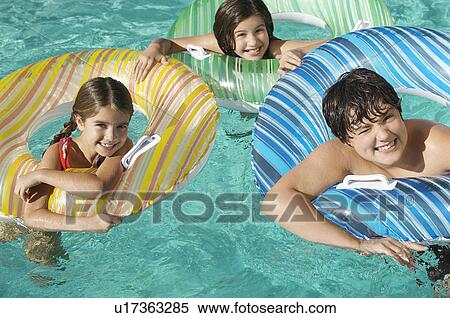 Stock Photography - Three children in inflatable rafts in swimming pool, portrait. Fotosearch