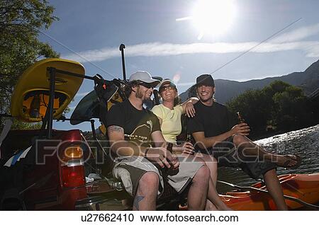 Stock Image - Three kayakers relaxing with beer. Fotosearch