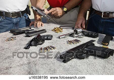 Stock Photography - Three men with table of guns, mid section, close-up. Fotosearch