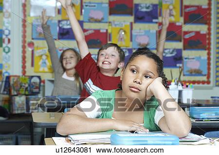 Stock Image - Three pupils in classroom, two with raised hands, one pensive. Fotosearch