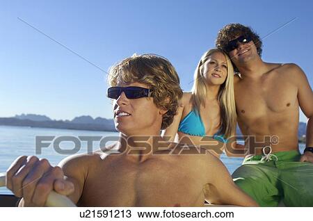 Stock Image - Three young friends relaxing in boat on lake. Fotosearch