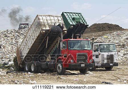 Stock Image - Trucks dumping waste at landfill site. Fotosearch