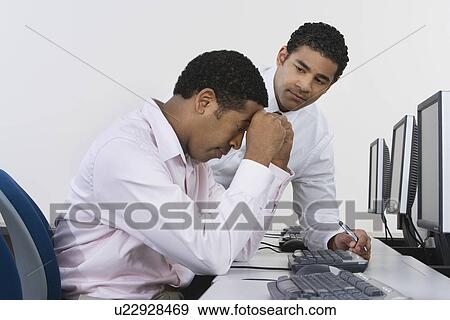 Stock Photo - Two business men at desk in front of computer. Fotosearch