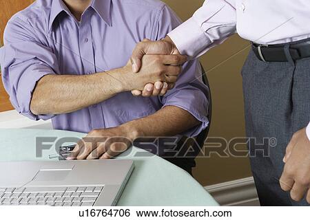 Stock Photograph - Two business men shaking hands in office, mid section. Fotosearch