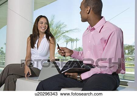 Stock Image - Two business people sitting outdoors with dayplanner and laptop. Fotosearch