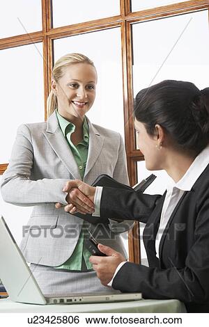 Stock Photograph - Two business women shaking hands in office. Fotosearch