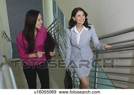 Stock Photo - Two business women walking up staircase in office building, elevated view. Fotosearch