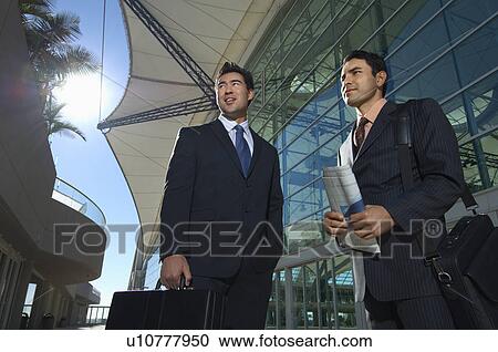 Stock Image - Two businessmen standing outside office building, low angle view. Fotosearch