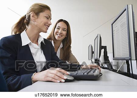 Stock Photo - Two businesswoman smiling over computers on table. Fotosearch