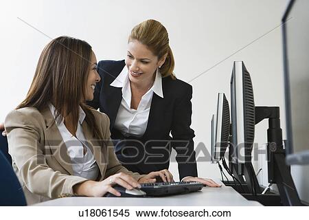 Stock Photography - Two businesswoman smiling over computers on table. Fotosearch