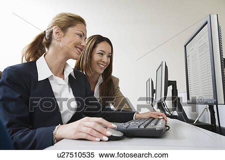 Stock Photography - Two businesswoman smiling over computers on table. Fotosearch