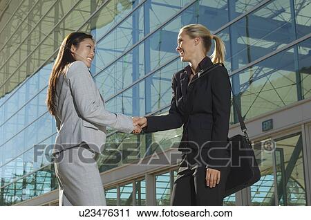 Two businesswomen shaking hands outside office building View Large Photo Image Stock Image - Two businesswomen shaking hands outside office building. Fotosearch
