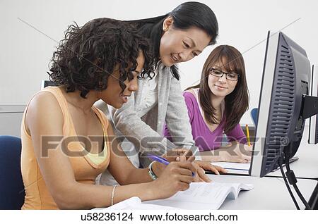 Picture - Two female students working with teacher in computer classroom. Fotosearch