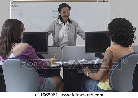 Two female students working with teacher in computer classroom View Large Photo Image Stock Image - Two female students working with teacher in computer classroom. Fotosearch