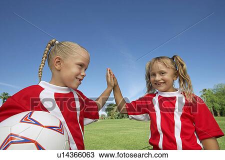 Stock Image - Two girl soccer players (7-9 years) doing 'high five' on soccer field. Fotosearch