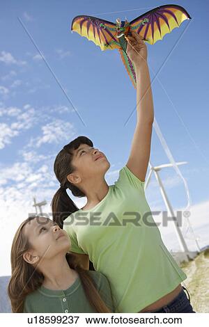 Stock Photo - Two girls (5-9) playing with kite at wind farm. Fotosearch