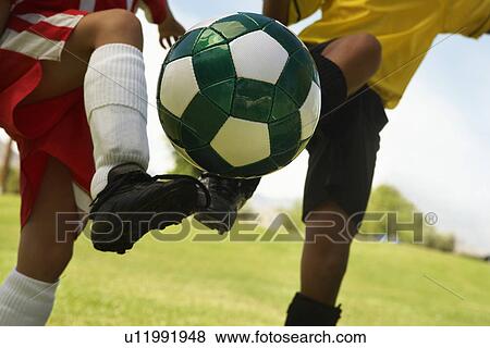 Stock Photo - Two little league players (7-9 years) kicking ball mid air, mid section, close up. Fotosearch