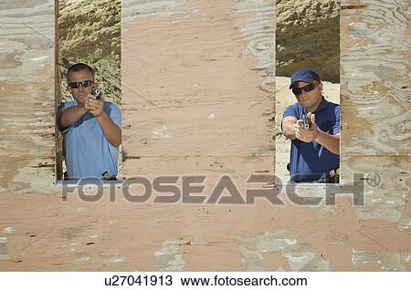 Stock Image - Two men aiming hand guns at firing range. Fotosearch