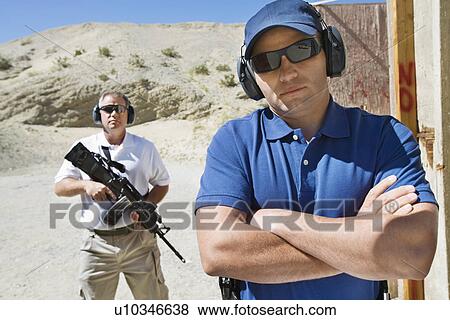 Stock Photo - Two men at firing range in desert, portrait. Fotosearch