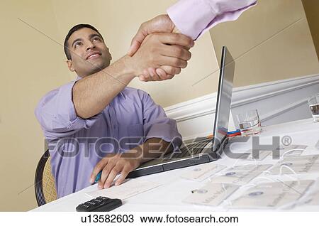 Stock Image - Two men shaking hands over desk with name tags. Fotosearch