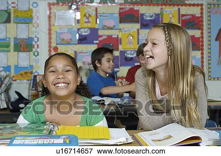 Two schoolgirls sitting at desk and laughing View Large Photo Image Stock Photo - Two schoolgirls sitting at desk and laughing. Fotosearch
