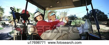 Stock Image - Two senior women laughing in golf cart. Fotosearch