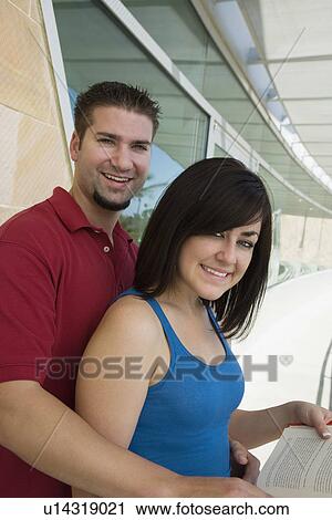 Stock Image - Two students holding books at school, smiling, portrait. Fotosearch