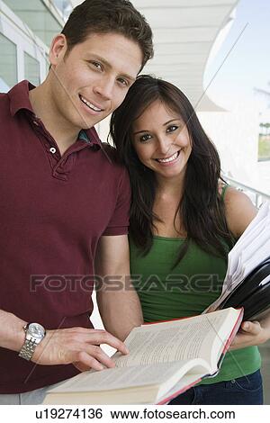 Stock Photograph - Two students holding books at school, smiling, portrait. Fotosearch