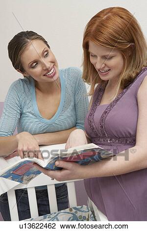Two women looking at book by cradle View Large Photo Image Stock Image - Two women looking at book by cradle. Fotosearch