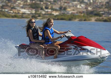 Stock Image - Two young women riding jetski on lake. Fotosearch
