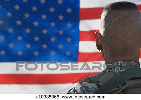 Stock Photograph - US Army soldier looking at flag, back view. Fotosearch